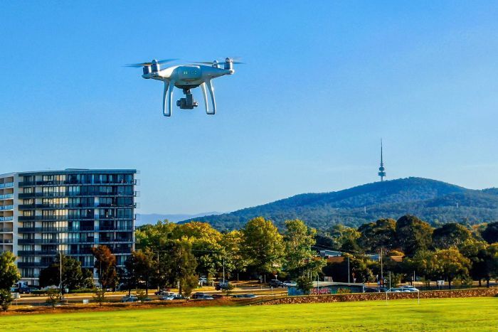 A drone flying above a playing field in Canberra. An apartment building and Black Mountain Tower is in the background.