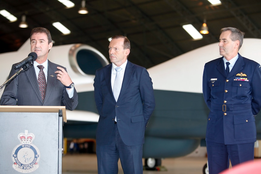 Three man stand in a row, with former prime minister Tony Abbott in centre, 