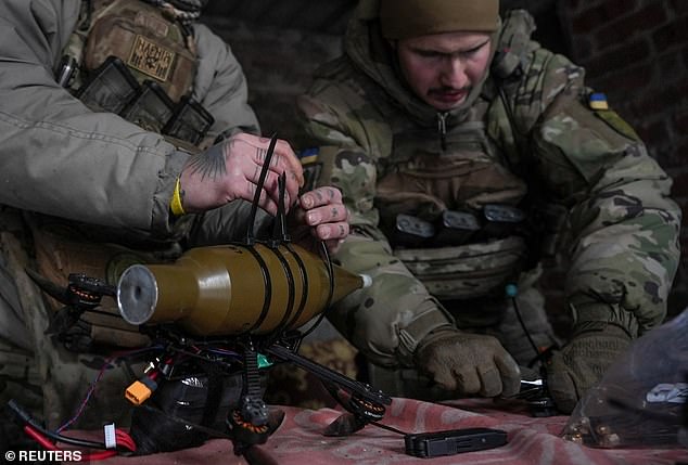 A Ukrainian operator straps an explosive warhead to a drone inside a bunker on the front line