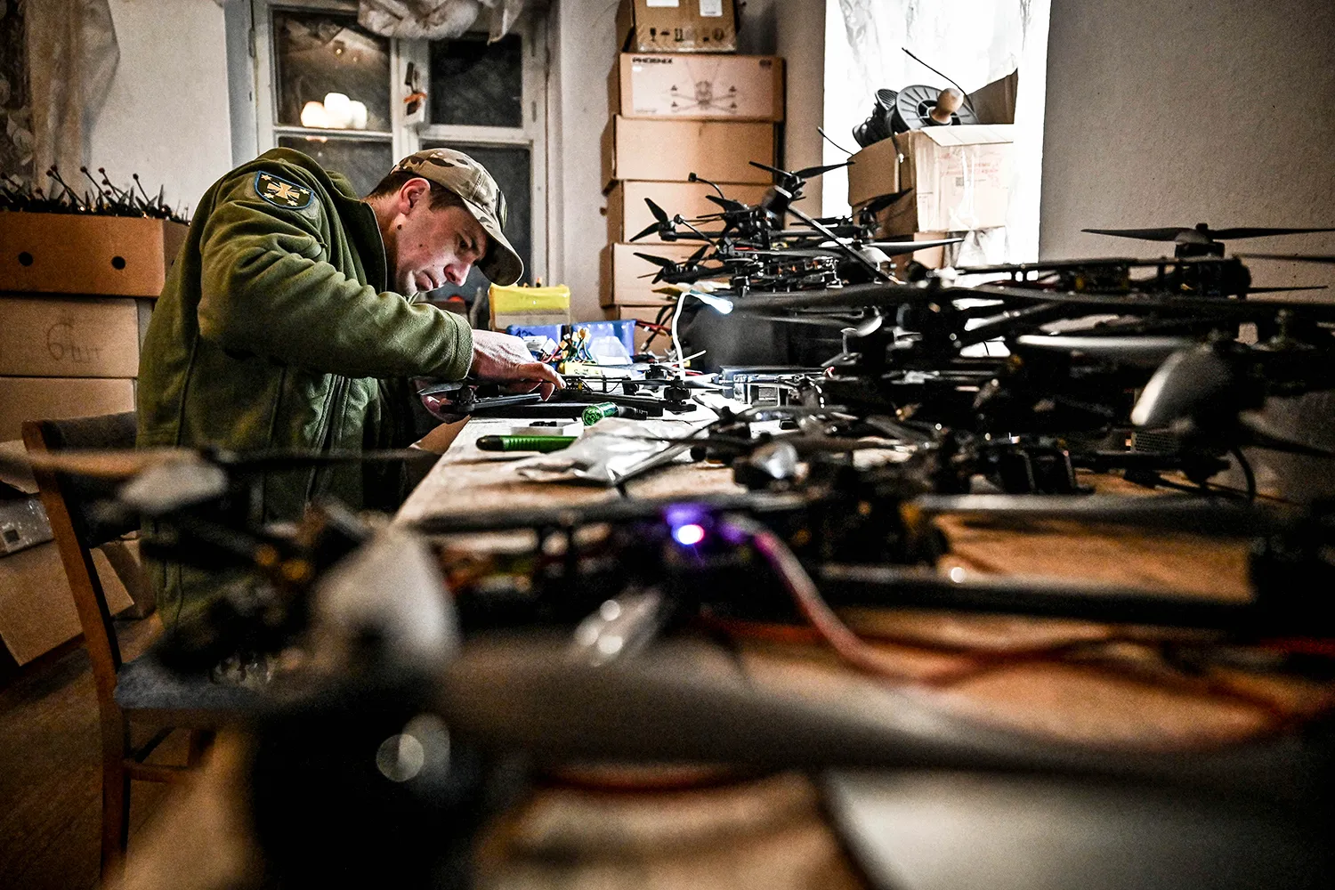 A serviceman is assembles a drone, surrounded by many drones in the workshop.